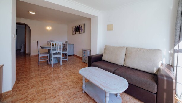 A living room with a brown sofa, a white coffee table, and a dining area with a table and chairs. - Villa Benicuco 24 - PlusHolidays (Calpe)