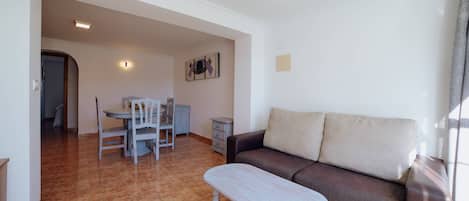 A living room with a brown sofa, a white coffee table, and a dining area with a table and chairs.