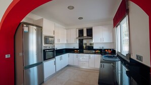 A modern kitchen with white cabinets, stainless steel appliances, and a black countertop. - Villa Benicuco 24 - PlusHolidays (Calpe)