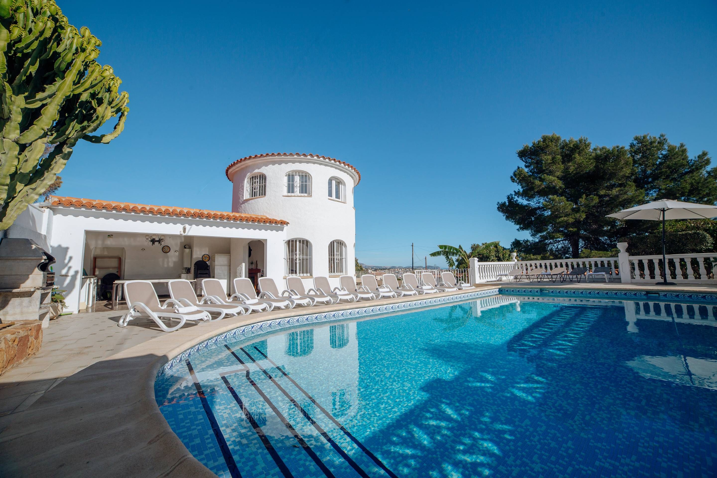 A pool area with a white building, lounge chairs, and a clear blue sky.