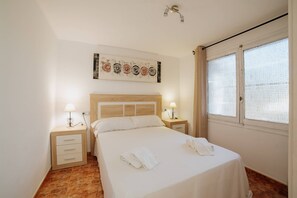 A hotel room with a bed, two bedside tables with lamps, a headboard, a window with curtains, and a wall art piece above the bed.