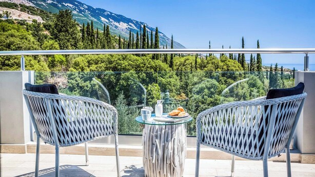 Ein Balkon mit zwei Korbstühlen, einem kleinen runden Tisch und Blick auf eine Berglandschaft.