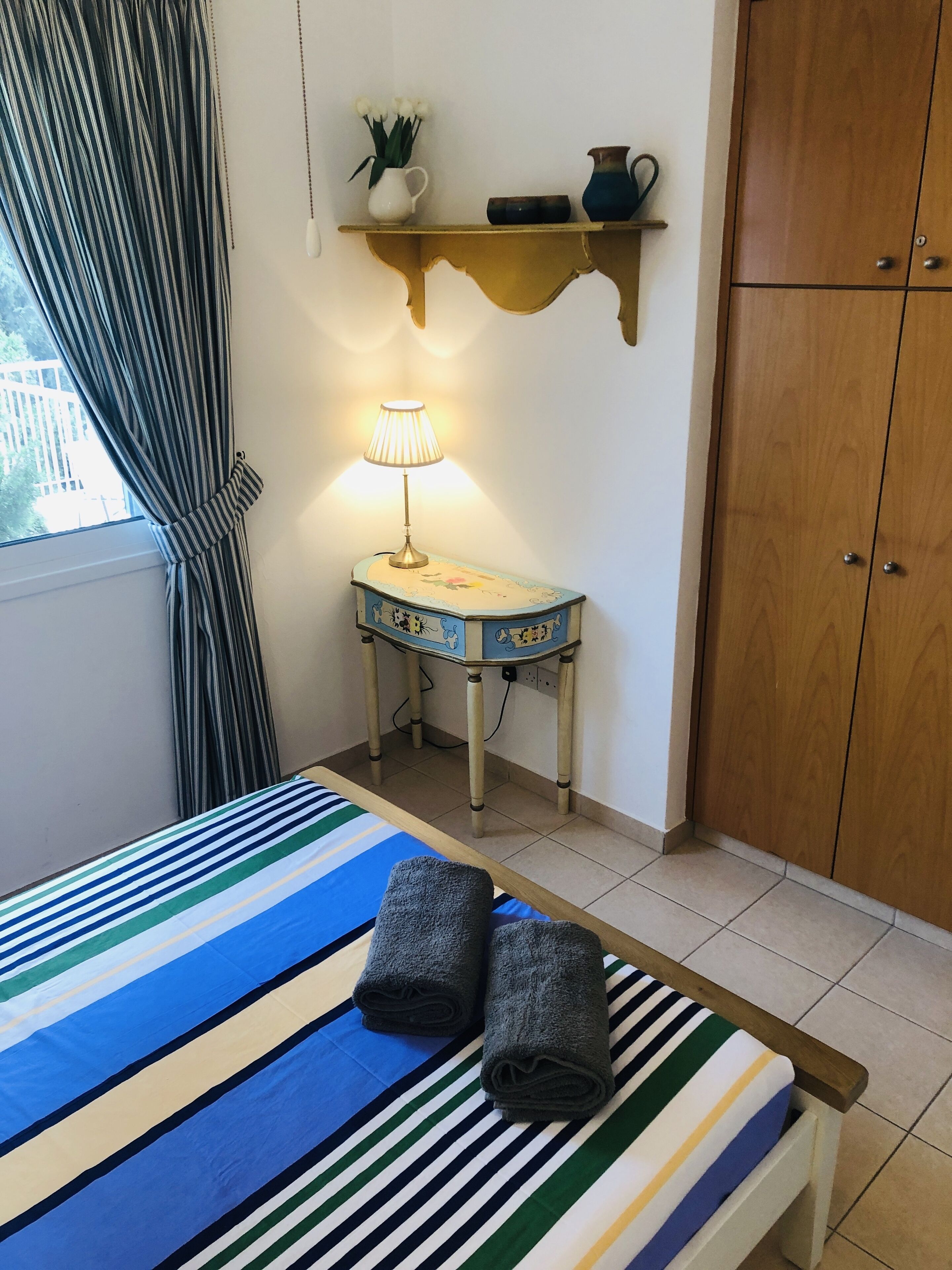 Ein Zimmer mit einem Bett, einem Nachttisch mit Lampe, einem Regal mit Dekoration und einem Kleiderschrank.