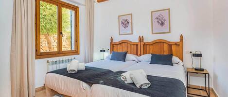 A double bed with a wooden headboard, two bedside tables, a window with curtains, and two framed leaf artworks on the wall.
