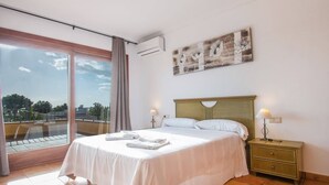 A hotel room with a bed, a nightstand, a lamp, a painting, and a view of the outdoors. - Apartment Topacio 1 - Plusholidays (Calpe)