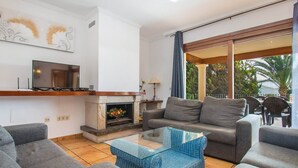 A modern living room with a fireplace, grey sofas, a glass coffee table, and a TV on a wooden shelf. - Apartment Topacio 1 - Plusholidays (Calpe)