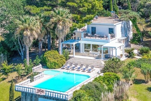 Una villa moderna con piscina, mobiliario exterior y exuberante vegetación.