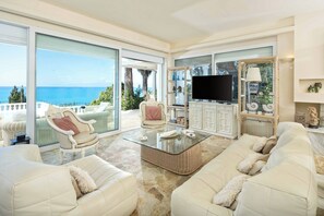 Un salón amplio con un gran ventanal que da a un balcón con vistas al mar.