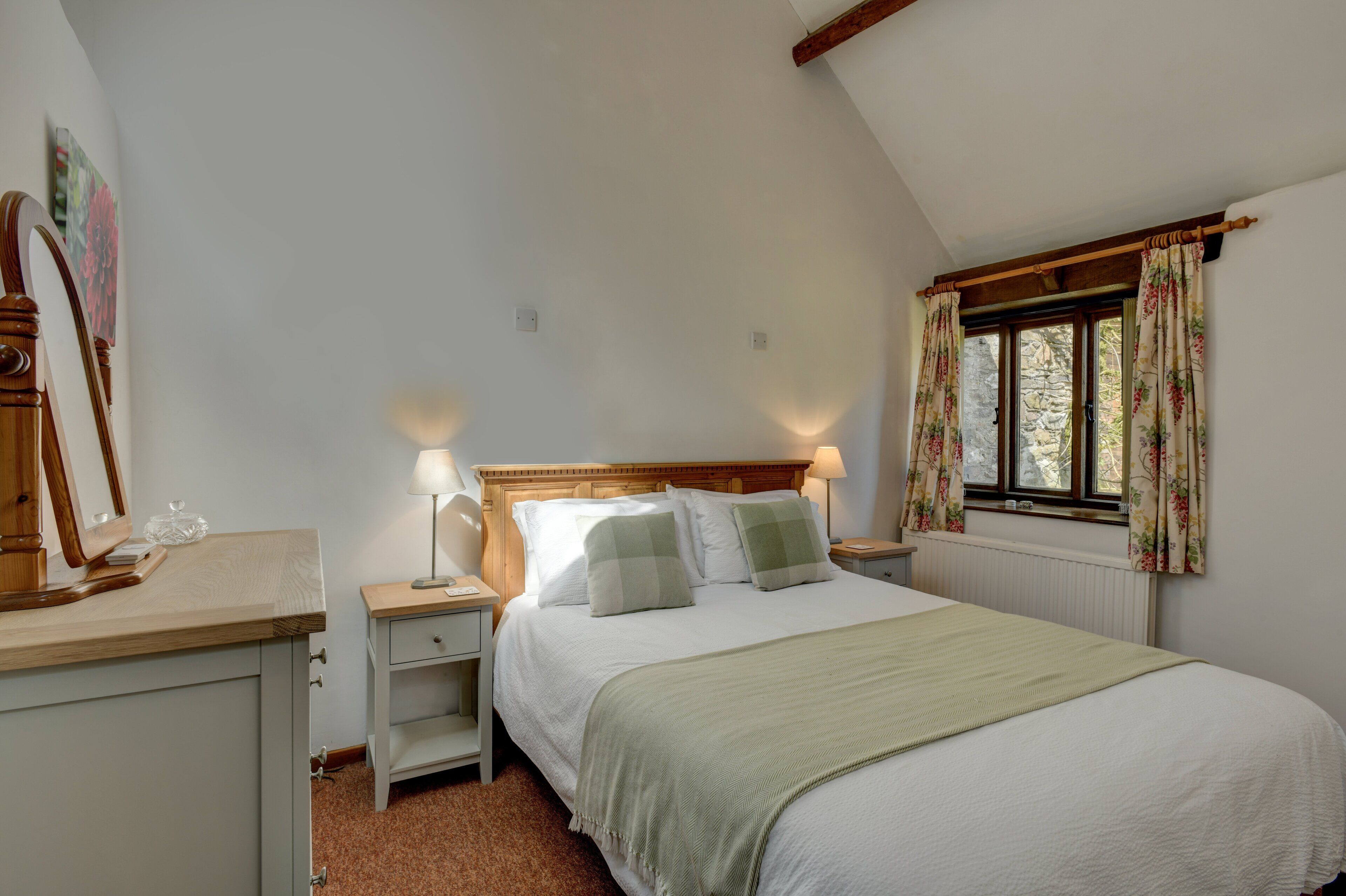 A bedroom with a bed, bedside tables, a nightstand, a dresser, a mirror, and a window with curtains.