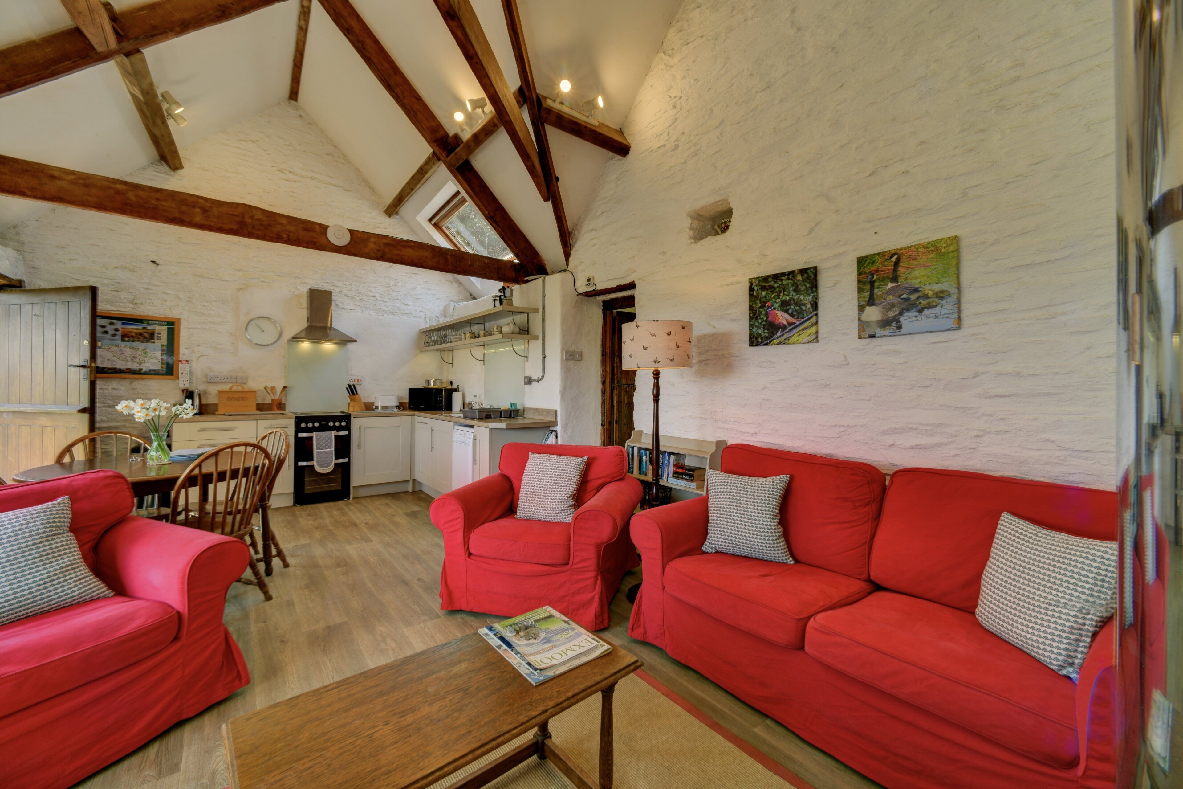 A spacious living area with red sofas, a wooden coffee table, and a kitchen in the background.
