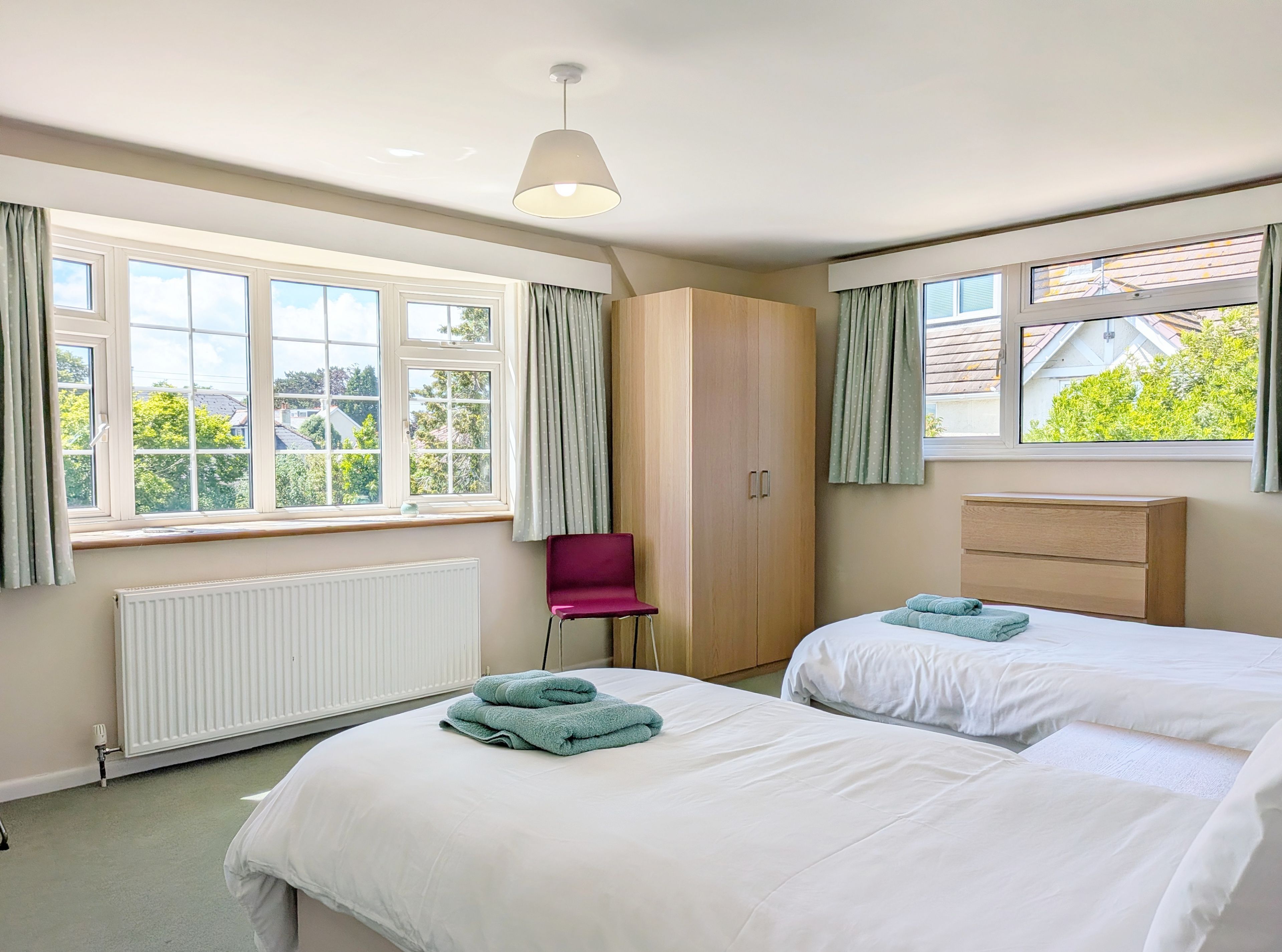 A hotel room with two beds, a wooden wardrobe, a radiator, and a window with curtains.