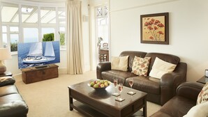 A living room with a brown leather sofa, a wooden coffee table with a bowl of fruit and two glasses, and a television displaying a sailboat. - Beach View, Southbourne, Nr Bournemouth , Dorset (Southbourne)