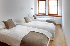 A room with two beds, each with white bedding and brown pillows, a standing lamp, and a window with a view of the outside.