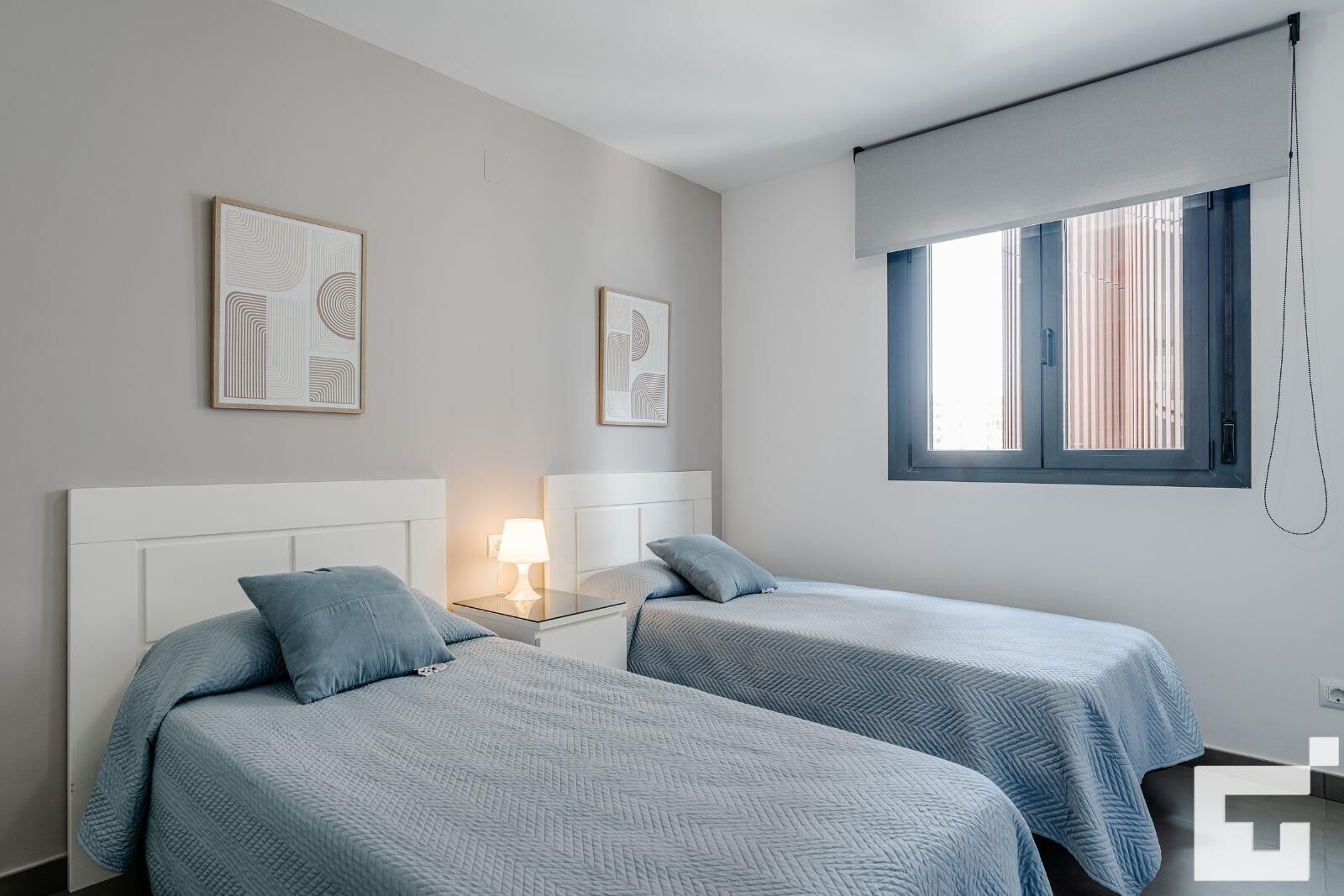 Ein Zweibettzimmer mit zwei Betten, einem Nachttisch mit Lampe und einem Fenster mit Jalousien.