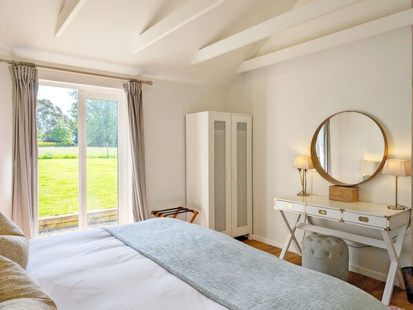 Une chambre à coucher avec un lit, un bureau doté d’un miroir, une armoire et une vue sur un jardin, visible par la fenêtre.