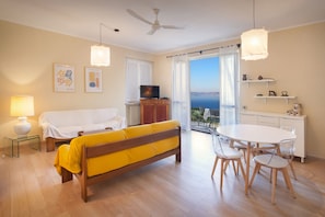 Relax in this stylish living room with a flat-screen TV, dining area, and sliding glass door leading to a balcony with a sea view.