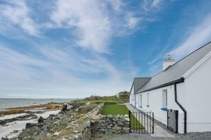 A coastal property with a white building, a stone wall, and a grassy lawn leading to the sea.