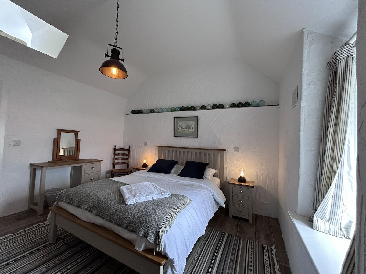 A bedroom with a bed, bedside tables, a dresser, a hanging light fixture, and a window with curtains.