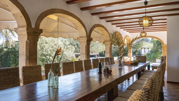 A long wooden table with a wine bottle and glasses, surrounded by cushioned chairs with a view of greenery outside. - Adsubia 12 - Javea, Costa Blanca (Javea)