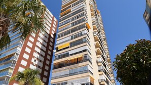 A tall building with multiple balconies, a restaurant at the ground level, and a palm tree in the foreground. - MIRAMAR PLAYA (STUDIO) (Benidorm)
