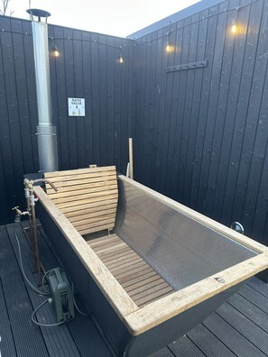 A hot tub with a wooden bench, surrounded by a dark wooden fence, with a sign indicating a bath valve.