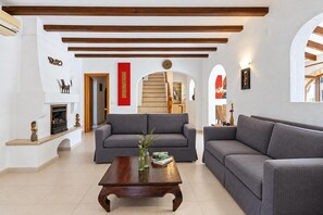 A spacious living room with two grey sofas, a wooden coffee table, and a fireplace. - Villa Escocia - Javea, Costa Blanca (Javea)