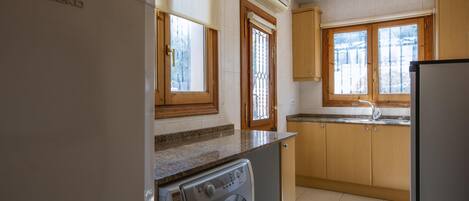 Una cocina con lavadora, refrigerador, armarios de madera, una ventana y un equipo de aire acondicionado.