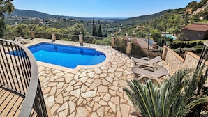 A swimming pool with stone tiles, lounge chairs, and a view of a valley.