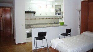 A compact kitchen with a built-in stove, a sink, and a countertop. There are two black chairs and a bed with white bedding. - LAS PALMERAS (STUDIO) BENIDORM (Benidorm)