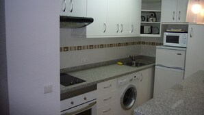 A compact kitchen with white cabinets, a washing machine, a microwave, and a sink. - LAS PALMERAS (STUDIO) BENIDORM (Benidorm)