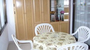 Un comedor con una mesa redonda cubierta con mantel, rodeada por cuatro sillas blancas. Detrás de la mesa, hay un aparador de madera con puertas de vidrio que exhibe diversos objetos.