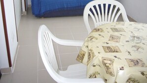 Una habitación con un sofá azul, dos sillas blancas, una mesa con mantel estampado y un cuadro enmarcado en la pared.