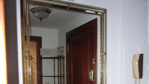 Un pasillo con un espejo grande que refleja una puerta, un teléfono y una planta en maceta.