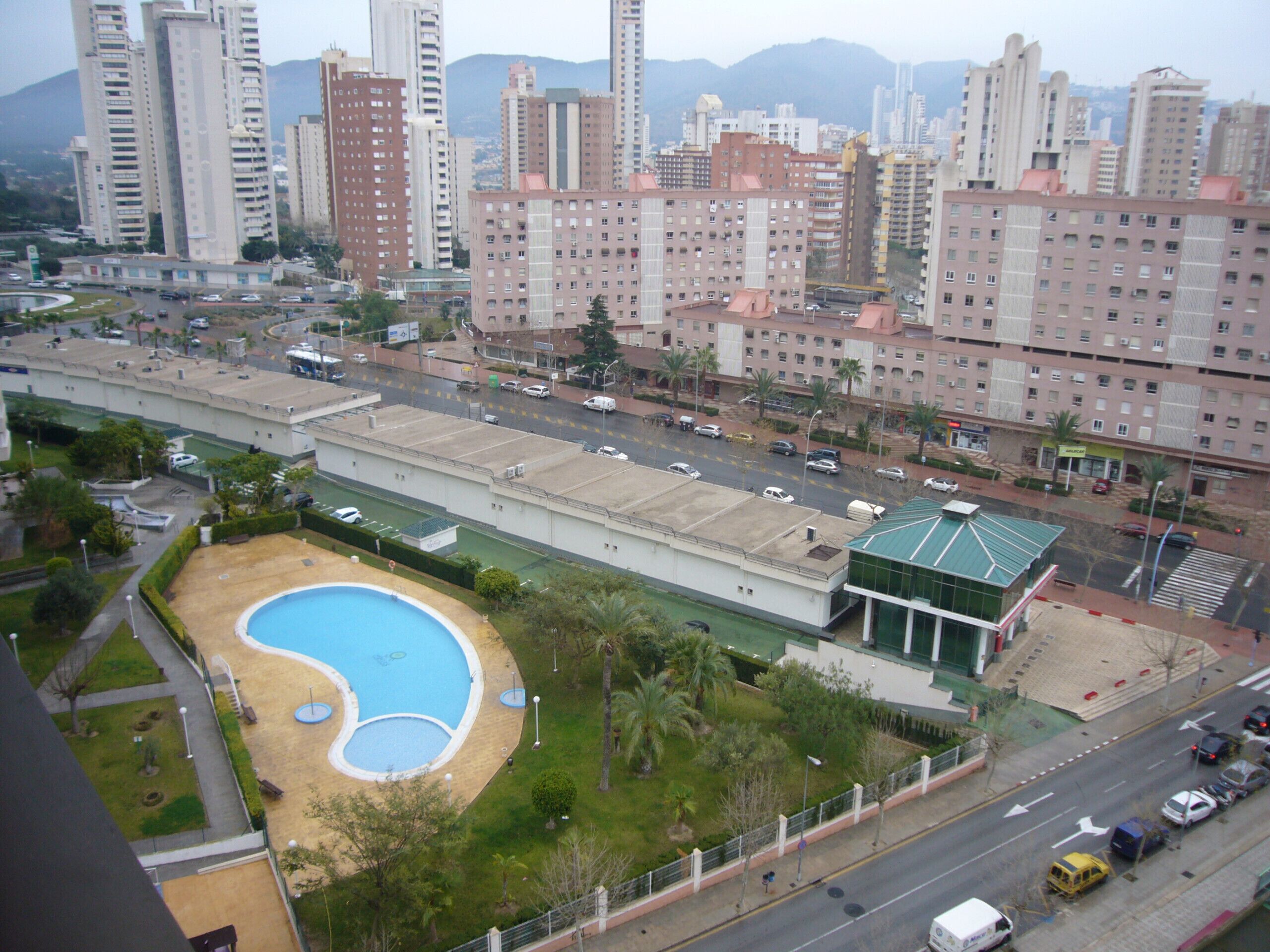 Un immeuble de grande hauteur, doté de nombreux étages, d’une piscine et situé le long d’une route où circulent des véhicules.