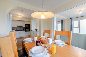 A dining area with a wooden table, chairs, plates, a glass of orange juice, a loaf of bread, and a jar of jam.