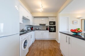 Een kleine keuken met witte kastjes, een wasmachine, een magnetron en een oven.