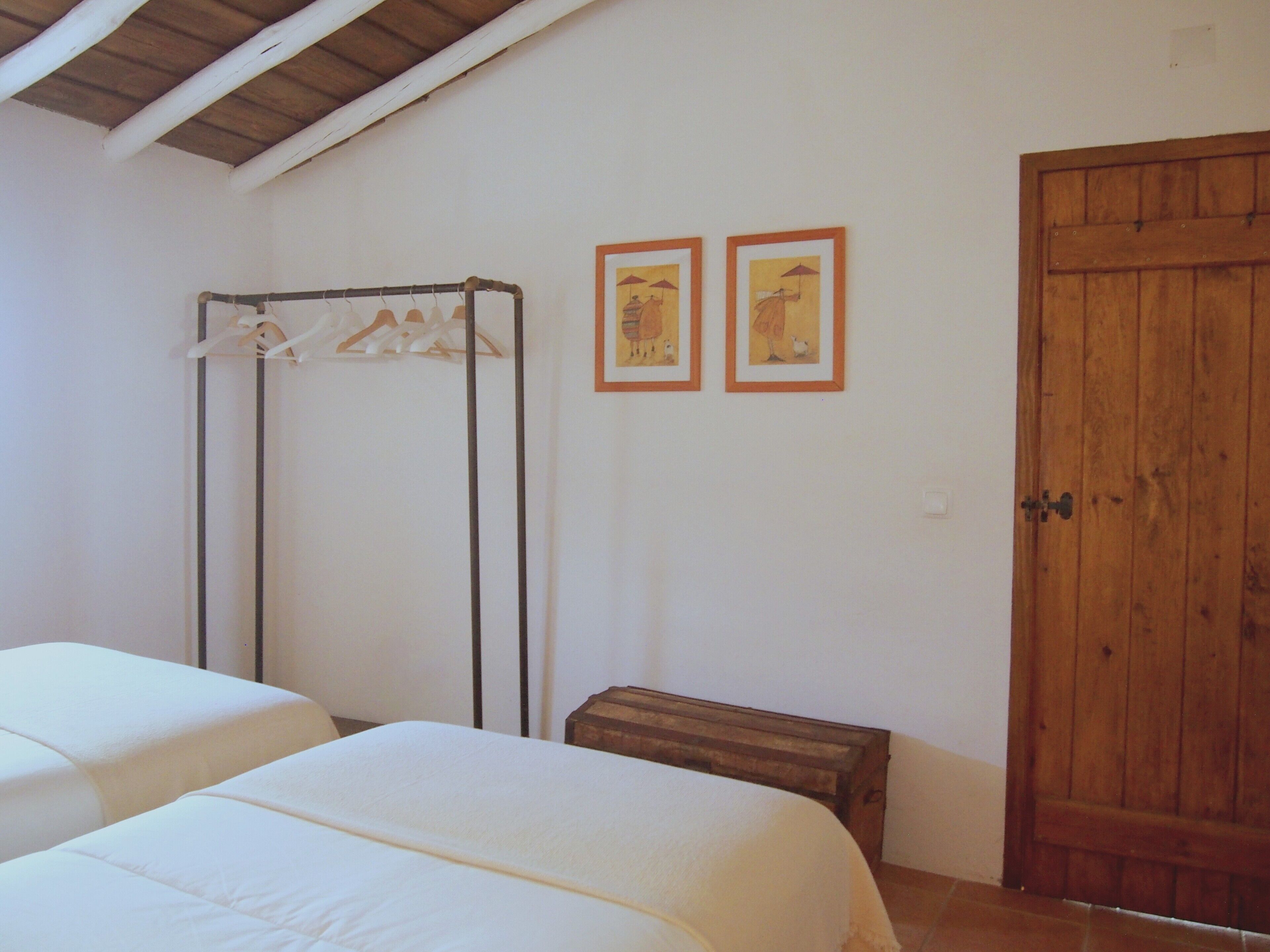 Een slaapkamer met twee bedden, een houten garderobe, een droogrek en twee ingelijste foto's aan de muur.