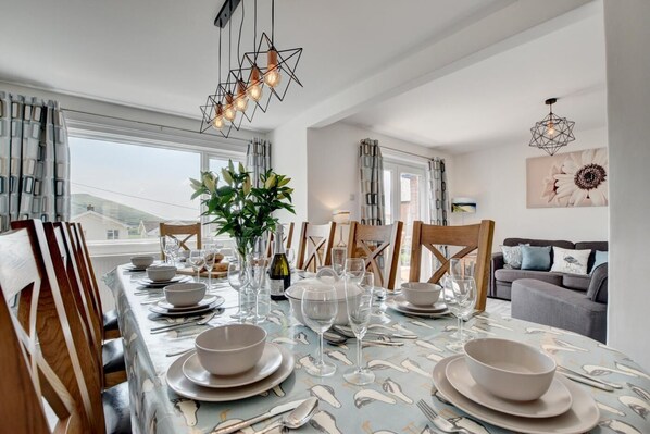 A dining area with a table set for four, a vase with flowers, and a modern chandelier.