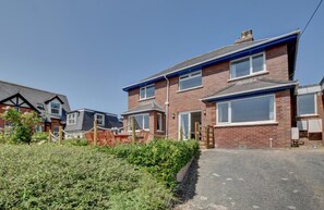 A two-story residential building with a paved driveway, a wooden fence, and a garden area.