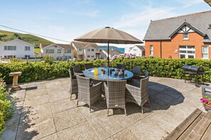 A patio with a round table and chairs, a grill, and a stone pillar.
