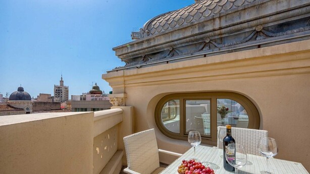 Terraço no telhado com mesa posta para dois, incluindo uma garrafa de vinho, dois copos e uma travessa de uvas.
