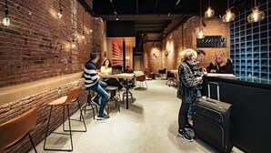 A modern cafe with brick walls, wooden tables, and hanging pendant lights.
