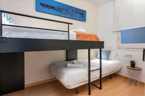 Habitació amb literes, una finestra, una taula petita amb una planta i un quadre penjat a la paret.