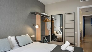 A modern hotel room with a large bed, a wardrobe, a mirror, and a small ironing board.
