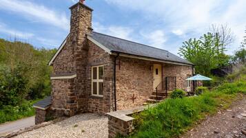 Une maison en pierre avec une cheminée, un petit porche et une allée gravillonnée.