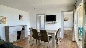 A dining area with a table and chairs, a television mounted on the wall, and a sofa in the foreground. - ROCAMAURA I-A-3-1 (Estartit)