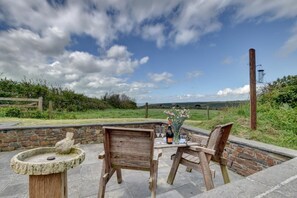 A patio with stone walls, a wooden table, two chairs, and a birdbath.