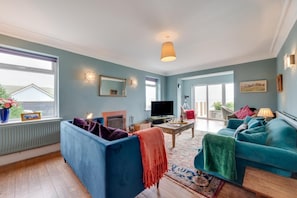 A living room with a fireplace, a television, and a large window overlooking a balcony. - 4 Bed in Woolacombe (oc-n2116) (Woolacombe)