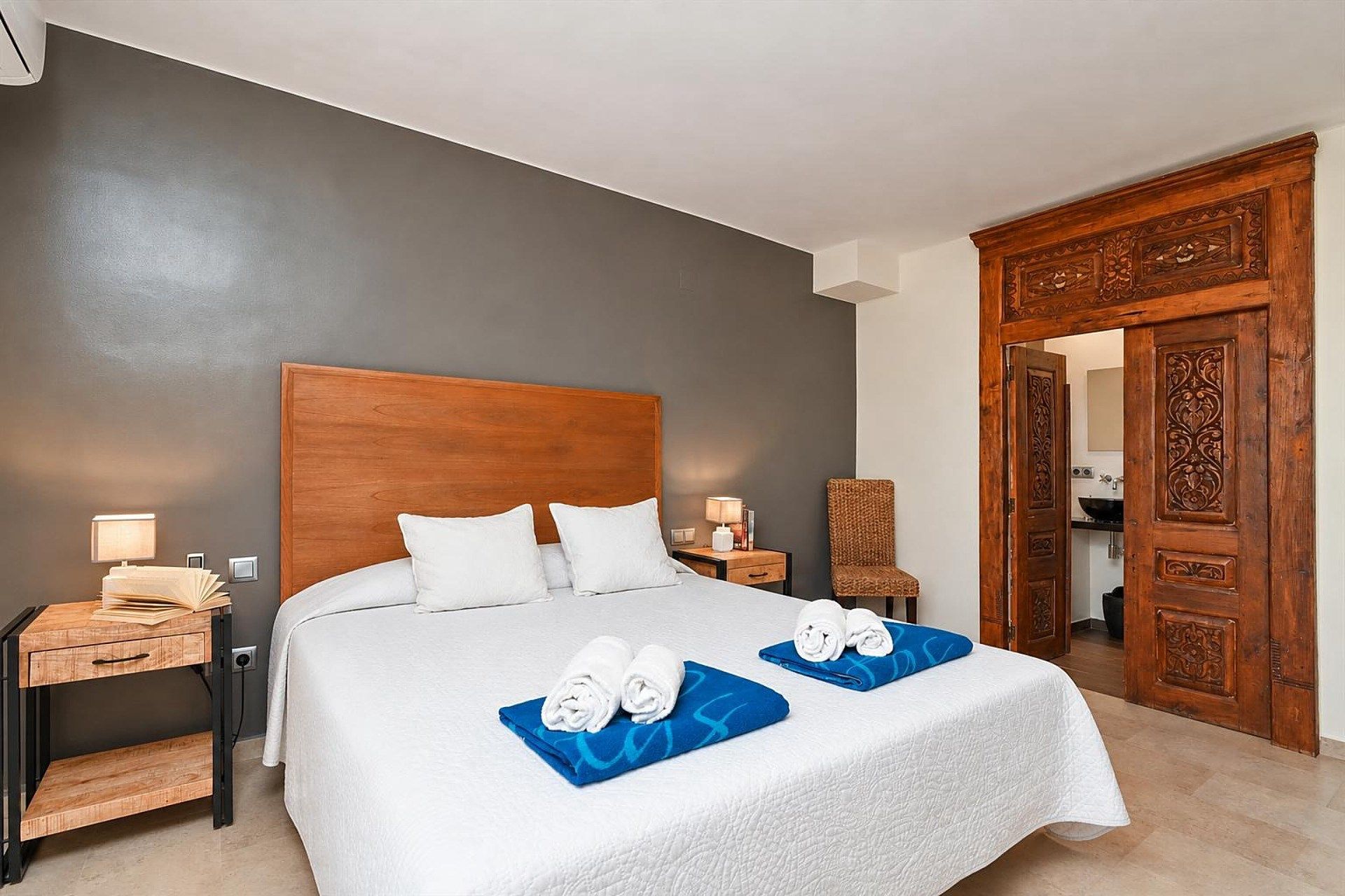 A hotel room with a large bed, two bedside tables, a wooden wardrobe, and a bathroom visible through an open door.