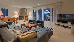 Een moderne woonkamer met een open haard, comfortabele zithoek, een eethoek en een grote televisie.